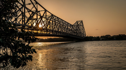 Silhouette of Howrah Bridge at the time of Sunrise.  People bathing and making rituals in the River Ganges.