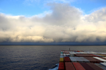 Container ship sailing towards cloudy horizon.