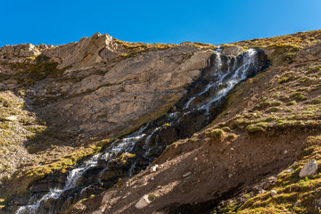 Water stream starts to melt from the summits snow and flows along it steep slopes making amazing waterfalls inside central Andes mountains. Amazing view of the huge rugged terrain Andes valleys scenic