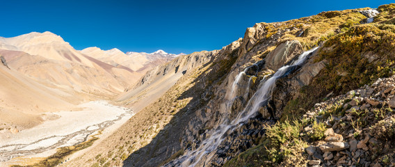 Fototapeta na wymiar Water stream starts to melt from the summits snow and flows along it steep slopes making amazing waterfalls inside central Andes mountains. Amazing view of the huge rugged terrain Andes valleys scenic