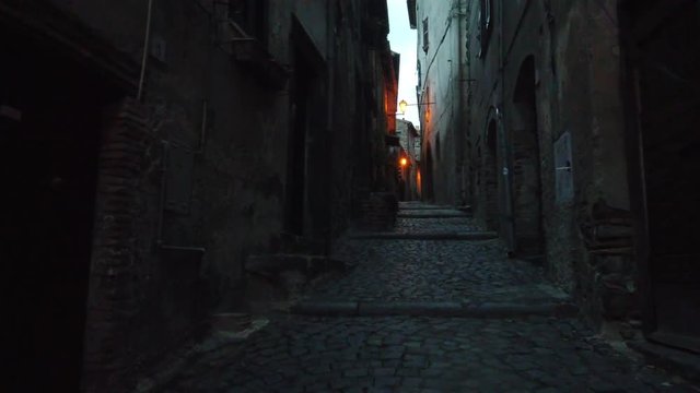 There is a little alley between houses, the road is a stone road by night. We are in a little old town near Rome. The place is called Bracciano.