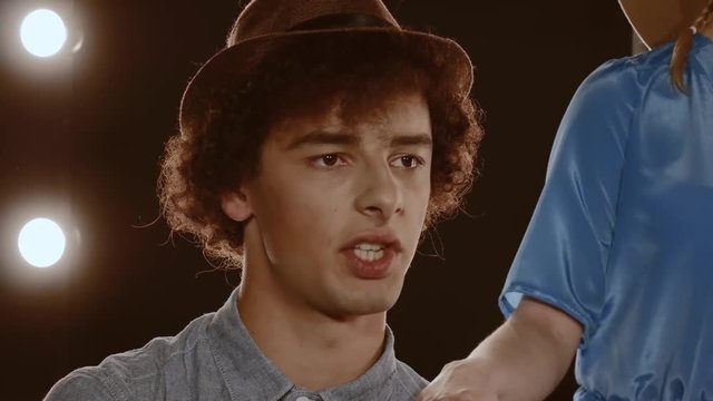 Guy beatboxer with curly hair in a hat, against a background of bright lights. Closeup portrait of a young man performing a beatbox