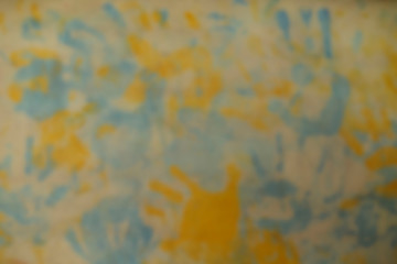 Fototapeta premium Blurred background. Abstracted surface texture of the wall with yellow and blue prints of children's palms. Cropped shot, horizontal, nobody, top view, place for text.