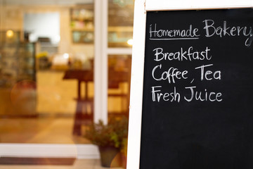 Close up beautiful hand writing menu on blackboard.Black chalk board in front of a coffee shop entrance.Blurred bakery and cafe background.Small business starting or shopping promotion concept.