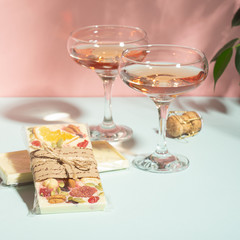 Drink champagne or wine in two elegant glasses and a bar of white chocolate. Gentle pink background bright sunlight.
