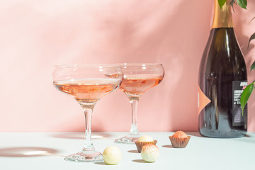 Naklejka premium Champagne or wine in elegant glasses, a box of chocolates pink background of bright light. Copy space. Selective focus.