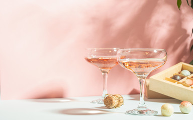 Champagne color or wine in glasses, box of white and dark chocolate candies on pink background bright light. Copy space.