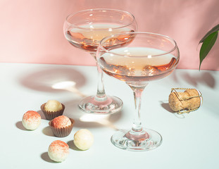Champagne or wine in elegant glasses various chocolates of white chocolate on a pink background hard light. Copy space.