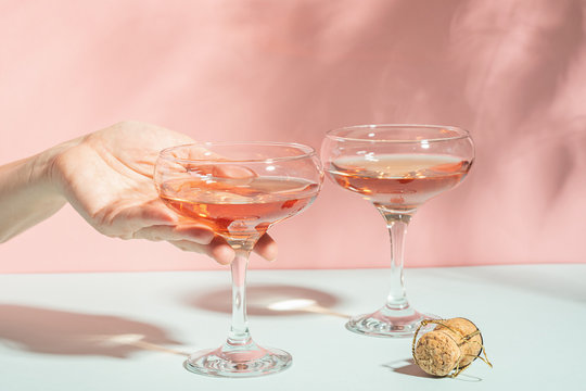 Female hand elegantly holding a glass of champagne or wine delicate pink background bright sunlight. Concept minimalism.