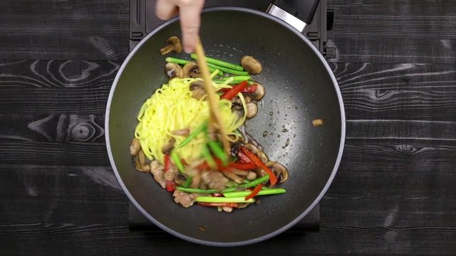 Stir fryed noodls with garlic sprouts and chopped pieces of mushrooms with chicken fried in oil in a wok pan. Cooking with champignons and fried noodles according to homemade recipe. Close.