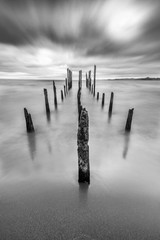 Like a highway to hell an old pier inside the lake waters under a dramatic overcast sky and high winds. The old wooden poles still fight against the elements under bad weather. Awe dramatic landscape