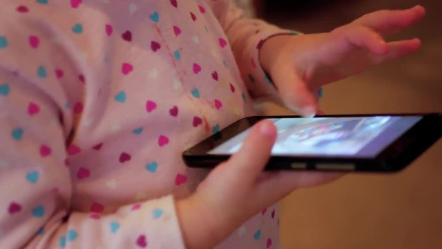Side view of a toddler swiping through pictures on a cellphone.