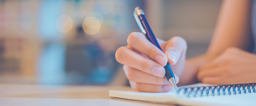 Woman hand is writing on a notepad with a pen in office.Web banner.