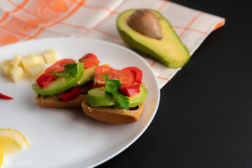 sandwiches with fresh organic avocado and red tomato on black surface, vegan breakfast