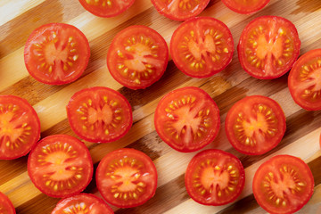 a lot of sliced in a half fresh red tomatoes on a cut board, vegeterian salad ingredientss