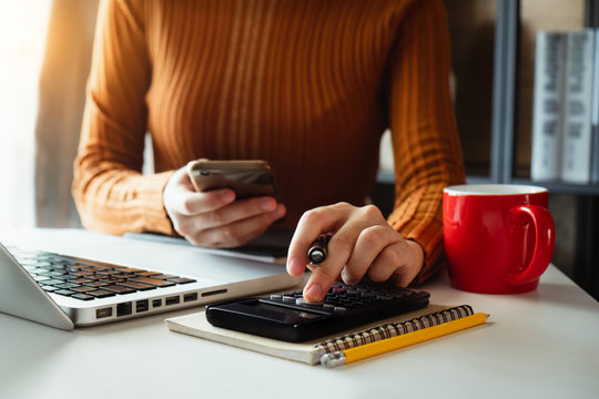 Businesswoman hands working with finances about cost and calculator and laptop with tablet, smartphone at office in morning light