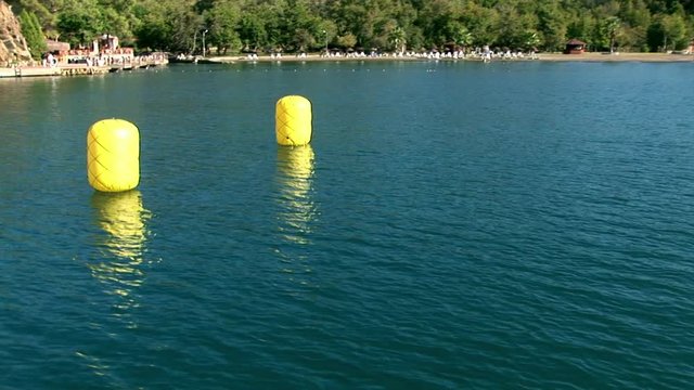 Yellow buoys for safety and orientation on water surface view from moving sailing yacht on background of mountain coast with green trees in summer during sea journey. Yachting as an active lifestyle.