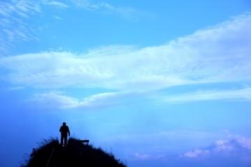 silhouette tourist standing alone on the top ,looking the beautiful blue sky background at Khao Chang Phueak,Kanchanburi
