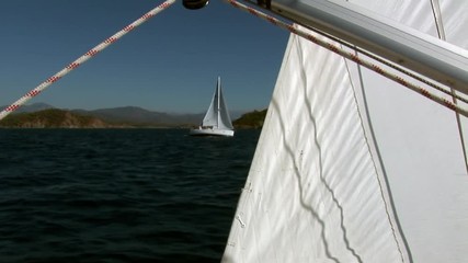 White sails, rope on sailing boat and details on deck of moving sailing yacht on background of water surface and sailing yacht moving away during sea journey. Yachting as an active lifestyle.