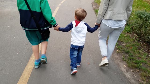 4k video of adorable smiling toddler boy holding by hand his mother and elder brother walking in park