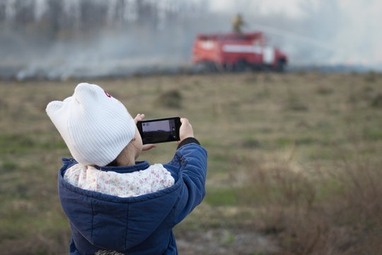girl shoots video on the phone as a fire engine puts out a forest fire