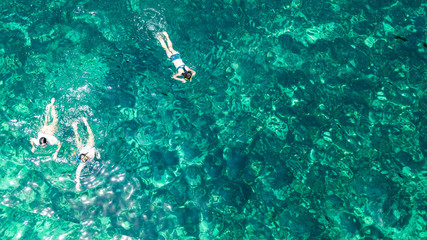 Aerial top view of family snorkeling from above, mother and kids snorkelers swimming in a clear tropical sea water with corals during summer vacation in Thailand