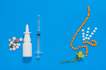 The figure of the nose of the tablets inhaling the fragrance of the flower and Allergy remedies on a blue background. Flat lay.
