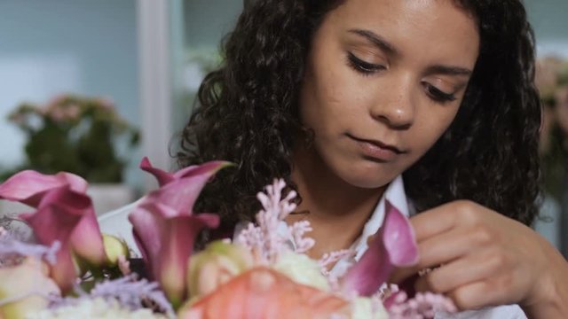 Closeup of gorgeous floral arrangement in hands of flowergirl satisfied with work done. Smiling mixed race woman florist finishing creation of stylish expensive bunch of fresh colorful exotic flowers