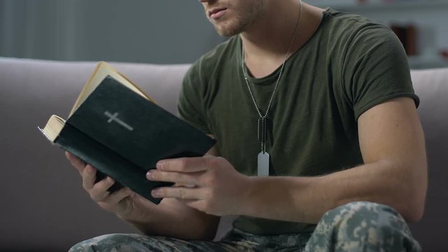 Young sergeant reading bible sitting on sofa, religious faith, hard time support