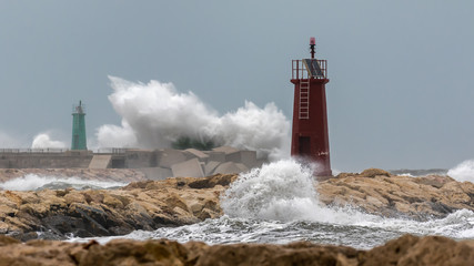 Big breakers in the storm hit the pier and the red and green lighthouse of the Spanish port city of...