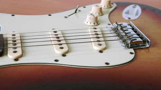 Slide motion of old electric guitar with a fine pattern of guitar strings placed on a wooden floor table