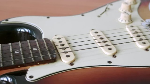 Slide motion of old electric guitar with a fine pattern of guitar strings placed on a wooden floor table