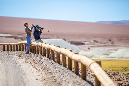Two women outdoor photographers taking photos at Andes Altiplano, awe mountain scenery at Atacama Desert. An arid landscape full of salt flats and lakes with beautiful volcanic scenery on a sunny day