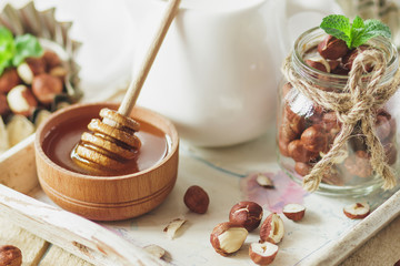 Honey in the wooden bowl, mint leaves, hazelnuts and jar with milk on the wooden tray