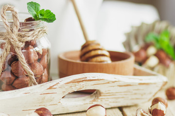 Honey in the wooden bowl, mint leaves, hazelnuts and jar with milk on the wooden tray