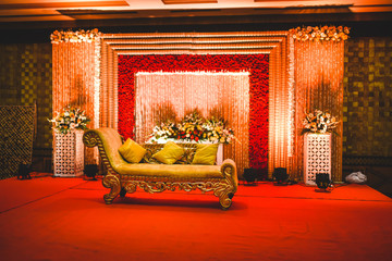 Huge stage at a wedding ceremony with beautiful yellow sofa for bride and groom. floral background lit by multiple stage lights.
