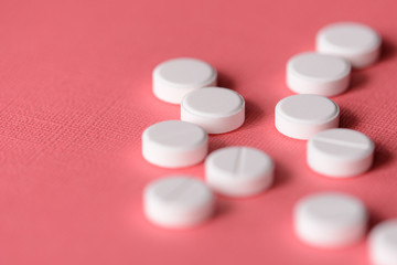 White tablets scattered on a pink background close up