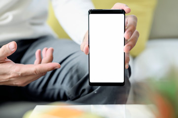 Cropped image of man holding and showing blank screen of smartphone while sitting at home.