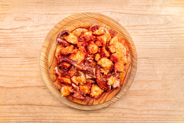 Pulpo a la gallega, an octopus with boiled potatoes and paprika, a typical Spanish Galician dish, on a traditional wooden plate, shot from the top on a wooden background with copy space