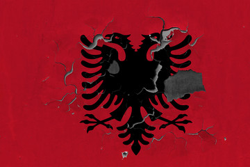 Close up grungy, damaged and weathered Albania flag on wall peeling off paint to see inside surface.