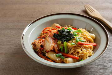 close up of stir fried egg noodles with kimchi in a ceramic dish on wooden table. asian homemade style food concept.