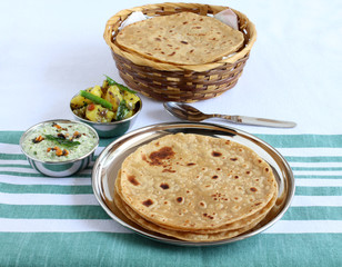 Chapati or Indian flat bread, which is a traditional and popular vegetarian breakfast or lunch item, with potato and onion curry and coconut chutney as side dishes, on a steel plate.