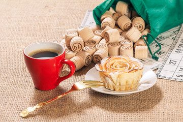 Board game lotto on sackcloth. Wooden lotto barrels in bag and game cards with cup of coffee and homemade cookie on plate.