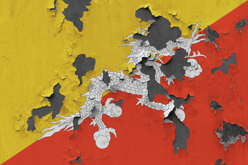 Close up grungy, damaged and weathered Bhutan flag on wall peeling off paint to see inside surface.