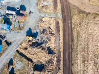 Aerial view of an excavator and yellow tractor transporting crushed stone, cement and sand during the extraction of minerals from the earth for the construction of roads and buildings on a sunny day.