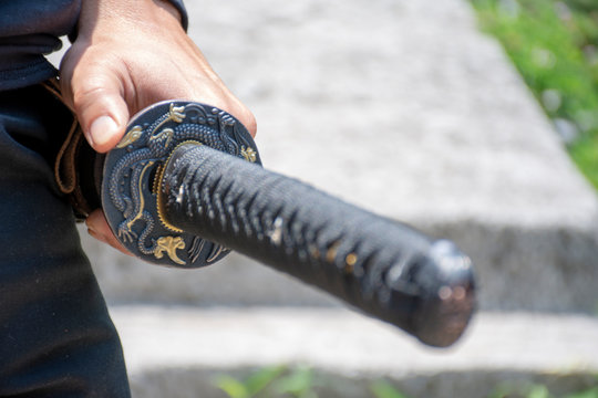 Imagen con un acercamieno de una katana, espada japonesa, en la mano, lista para atacar.