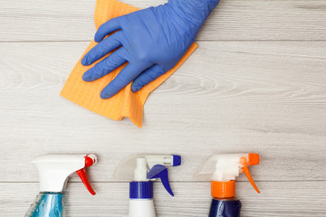 Hand in rubber glove holding dust napkin with bottles of detergent.