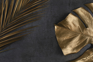 golden palm and monstera leaves on dark grey background © Aleksandra Konoplya