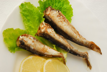 Pan-fried spiced sprats with lemon, salad on a plate