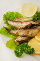 Pan-fried spiced sprats with lemon, salad on a plate
